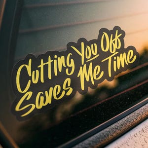 Puede incluir: Adhesivo negro con texto amarillo que dice "Cutting You Off Saves Me Time". El adhesivo está en la ventana de un coche, con un fondo borroso de luz solar. El adhesivo tiene un borde negro.