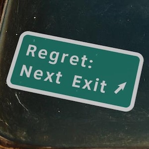 Puede incluir: Una pegatina rectangular verde con borde blanco y texto blanco que dice Regret: Next Exit, acompañada de una pequeña flecha blanca que apunta diagonalmente hacia arriba a la derecha, aplicada sobre el cristal oscuro de una ventana de vehículo.