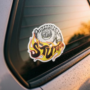 Puede incluir: Adhesivo con un diseño de turbocompresor y la palabra "STU" en una fuente con forma de llama. El adhesivo tiene un fondo blanco con detalles en negro, amarillo y rojo. Para entusiastas del automóvil.