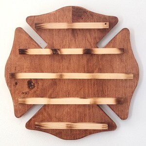 Puede incluir: Expositor de pared de madera con forma de cruz de Malta. El expositor tiene un acabado marrón oscuro con cuatro estantes horizontales de madera de color claro. Los bordes de los estantes tienen un aspecto quemado.