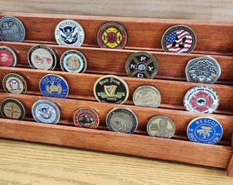 May include: A wooden coin display case with five rows of slots for holding challenge coins. The case is made of dark wood and has a beveled edge. The coins are a variety of colors and designs, including a fire department coin, a police department coin, and a military coin.
