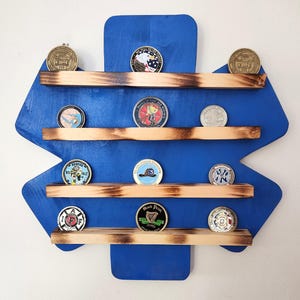 May include: A blue wooden star-shaped shelf with four shelves for displaying challenge coins. The shelves are made of natural wood with a burnt finish. The coins are displayed on the shelves, with some coins featuring a firefighter theme.