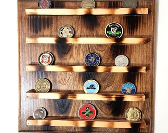Op de afbeelding: Een houten displayrek met vijf planken om challenge-munten te tonen. De planken zijn gemaakt van licht hout en hebben een donkerbruine vlek. De achtergrond is een lichtbruine muur.