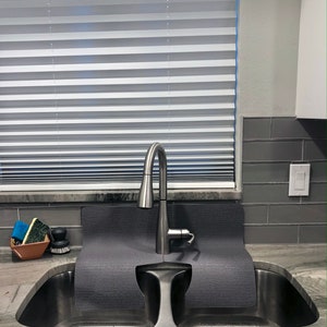 May include: A stainless steel kitchen sink with two basins. A gray silicone sink mat is placed over the basins. A silver faucet is mounted above the sink.