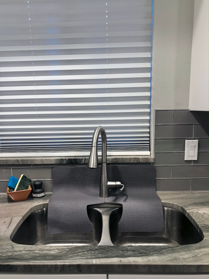 May include: A stainless steel kitchen sink with two basins. A gray silicone sink mat is placed over the basins. A silver faucet is mounted above the sink.