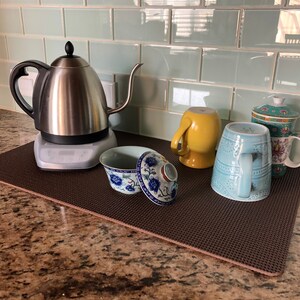May include: A stainless steel electric kettle with a gooseneck spout sits on a gray base, next to various mugs and a covered tea bowl. The mugs are yellow, light blue, and floral patterned. The tea bowl is white and blue.
