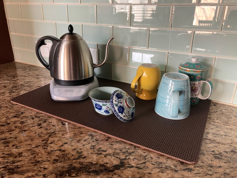 May include: A stainless steel electric kettle with a gooseneck spout sits on a gray base, next to various mugs and a covered tea bowl. The mugs are yellow, light blue, and floral patterned. The tea bowl is white and blue.