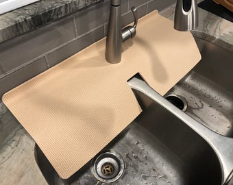 Könnte beinhalten: Eine beige Spülbeckenmatte mit strukturierter Oberfläche, die um einen Wasserhahn herum passt. Die Matte liegt über einem Doppelwaschbecken aus Edelstahl. Der Wasserhahn ist aus gebürstetem Nickel.