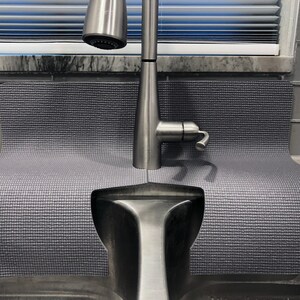 May include: A gray sink mat with a textured surface, designed to fit around a kitchen sink and faucet. The mat is made of a durable material and helps to protect the sink from scratches and dents.