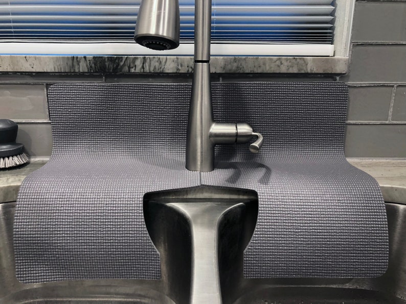 May include: A gray sink mat with a textured surface, designed to fit around a kitchen sink and faucet. The mat is made of a durable material and helps to protect the sink from scratches and dents.
