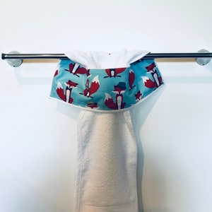 May include: A white towel with a blue and red fox print border hanging on a silver towel rail.