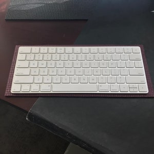 May include: A white wireless keyboard with a burgundy keyboard mat. The keyboard has a standard layout with function keys, arrow keys, and a numeric keypad. The keyboard mat has a textured surface.