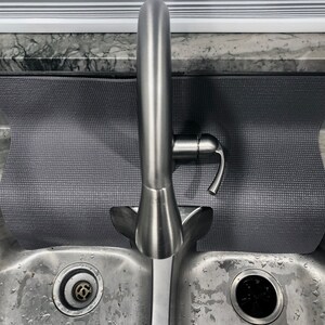 May include: A stainless steel kitchen sink with a gray sink mat and a single-handle faucet. The sink has two basins and a drain in each basin.