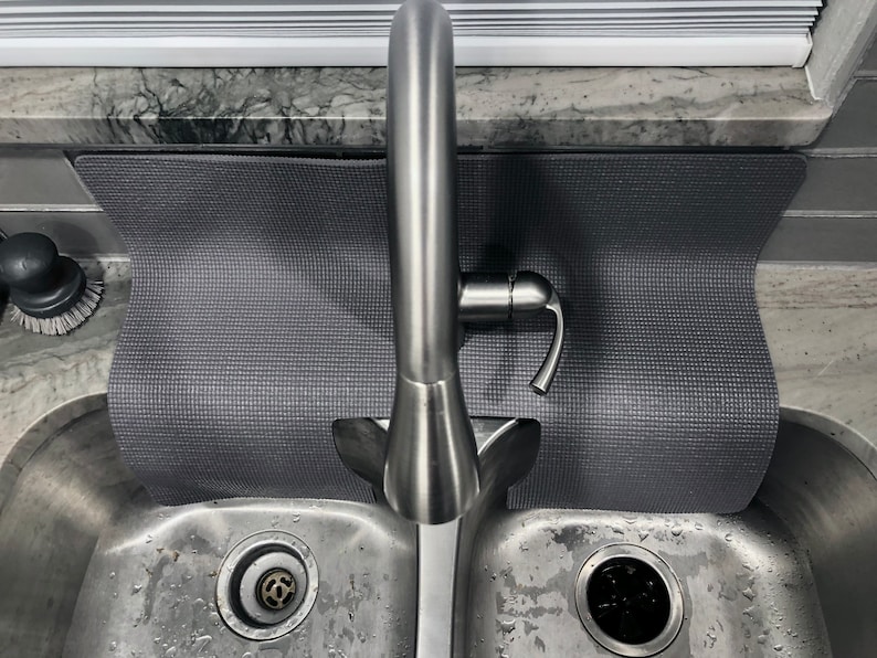 May include: A stainless steel kitchen sink with a gray sink mat and a single-handle faucet. The sink has two basins and a drain in each basin.