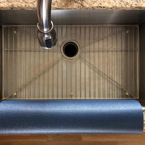 May include: A stainless steel kitchen sink with a metal grid and a rolled-up blue yoga mat. The sink is set into a granite countertop, with a chrome faucet above. The yoga mat is a textured, dark blue color.