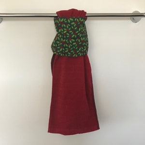May include: A red kitchen towel with a green holly and red berry pattern hanging on a silver towel rack.