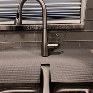 May include: A gray sink mat with a cut-out for a kitchen faucet. The mat is made of a textured material and is designed to protect the sink from scratches and damage.