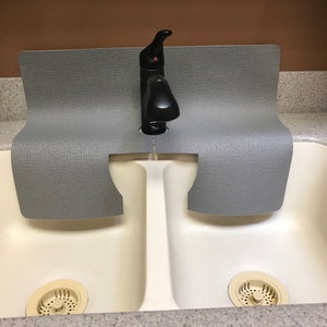 May include: A gray rubber sink mat with a cutout for a faucet, placed in a white double sink with two drain covers.