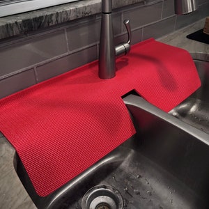 May include: Red silicone sink mat with a cut-out for the faucet, placed over a double stainless steel sink.