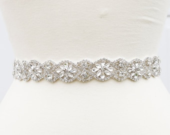 May include: A silver bridal belt with a crystal design. The belt is made of a delicate, flexible material and features a row of sparkling crystals.
