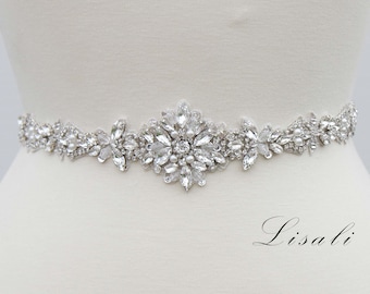 May include: A silver bridal belt with a large crystal and pearl embellishment. The belt is decorated with smaller crystals and pearls.