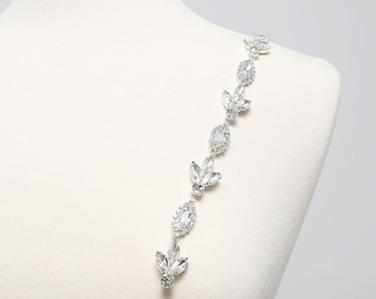 May include: A silver rhinestone strap with a leaf design. The strap is made of small, clear rhinestones that are connected together to form a chain. The chain is about 18 inches long and has a leaf-shaped design.