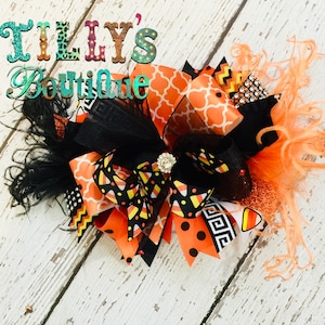May include: A large orange, black, and white Halloween hair bow with a candy corn pattern, black mesh, and orange feathers.