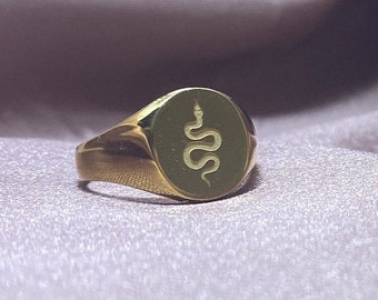 May include: A gold signet ring with a snake design engraved on the oval face.