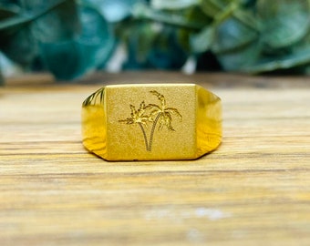 May include: A gold signet ring featuring a palm tree design.