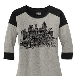 May include: A gray raglan-sleeve shirt with black sleeves and a black crew neck. The shirt features a detailed black and white illustration of a city skyline, with the word "Cleveland" and a signature printed below the skyline.