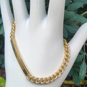Pode incluir: Um bracelete de corrente de ouro com um pequeno fecho retangular plano. A corrente é adornada com pequenas pedras transparentes.