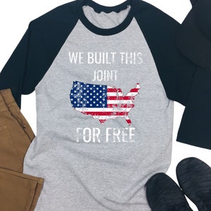 May include: A grey and black baseball tee shirt with a distressed American flag design and the text "We built this joint for free".
