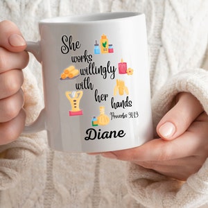 Könnte beinhalten: Weiße Keramiktasse mit einem Zitat über die Arbeit mit den Händen, illustriert mit Spa-Artikeln. Das Zitat lautet "She works willingly with her hands Proverbs 31:13" und der Name "Diane" ist darunter gedruckt.