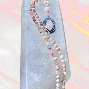 May include: A double-strand pink and white gemstone mala necklace with a large oval pink gemstone pendant set in a silver bezel with blue accents.