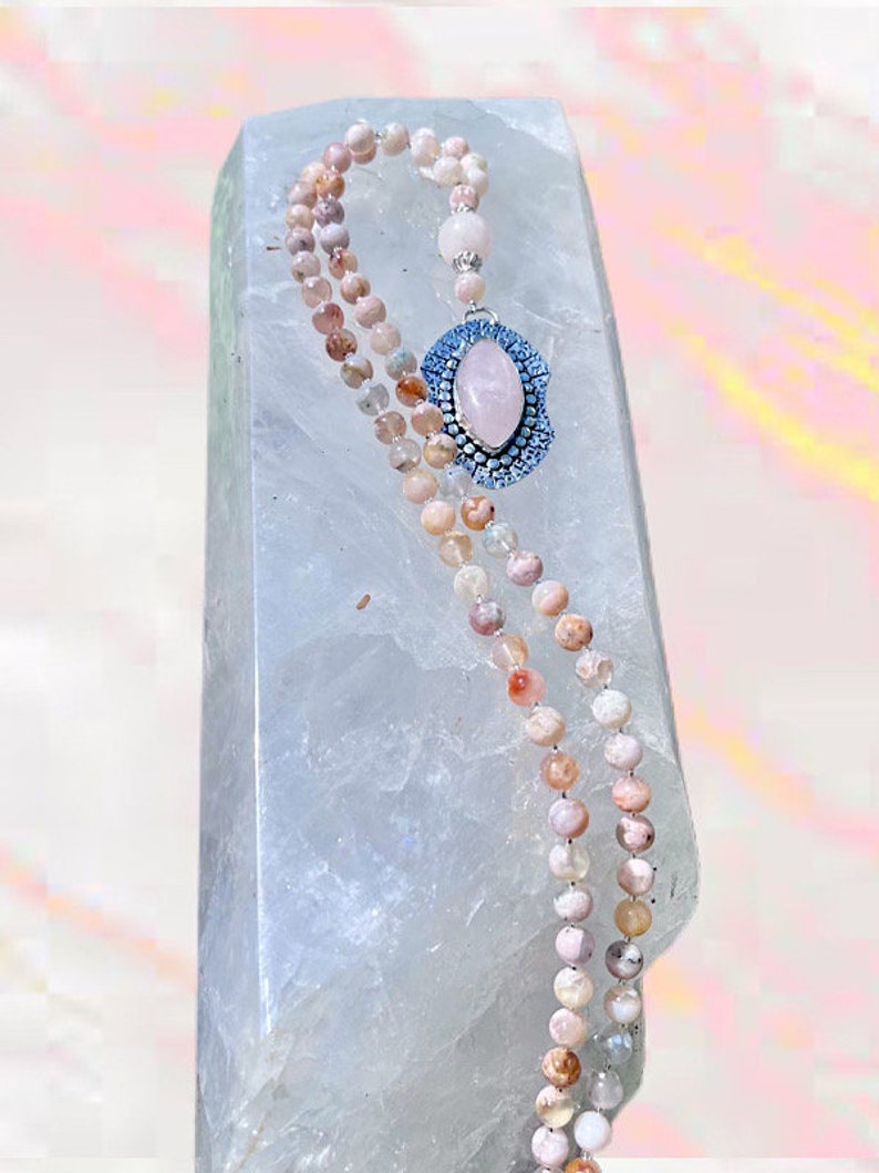 May include: A double-strand pink and white gemstone mala necklace with a large oval pink gemstone pendant set in a silver bezel with blue accents.