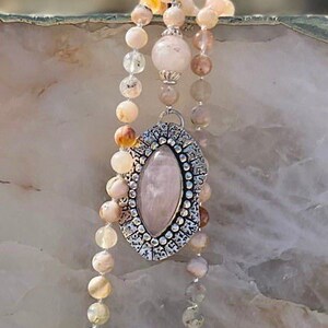 May include: A pink and white gemstone pendant necklace with a silver filigree design. The necklace is made with a variety of beads, including pink, white, and brown.