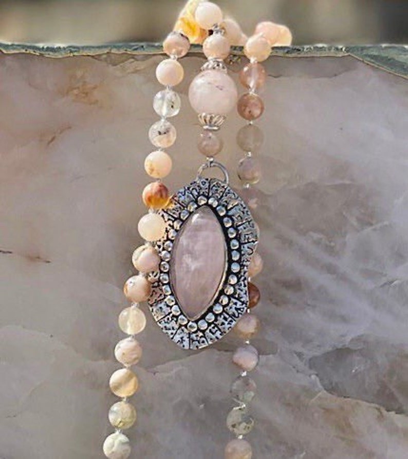 May include: A pink and white gemstone pendant necklace with a silver filigree design. The necklace is made with a variety of beads, including pink, white, and brown.