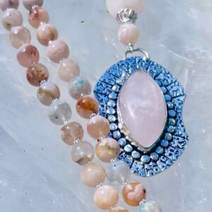 May include: A pink and white agate beaded necklace with a silver pendant featuring a large rose quartz stone.