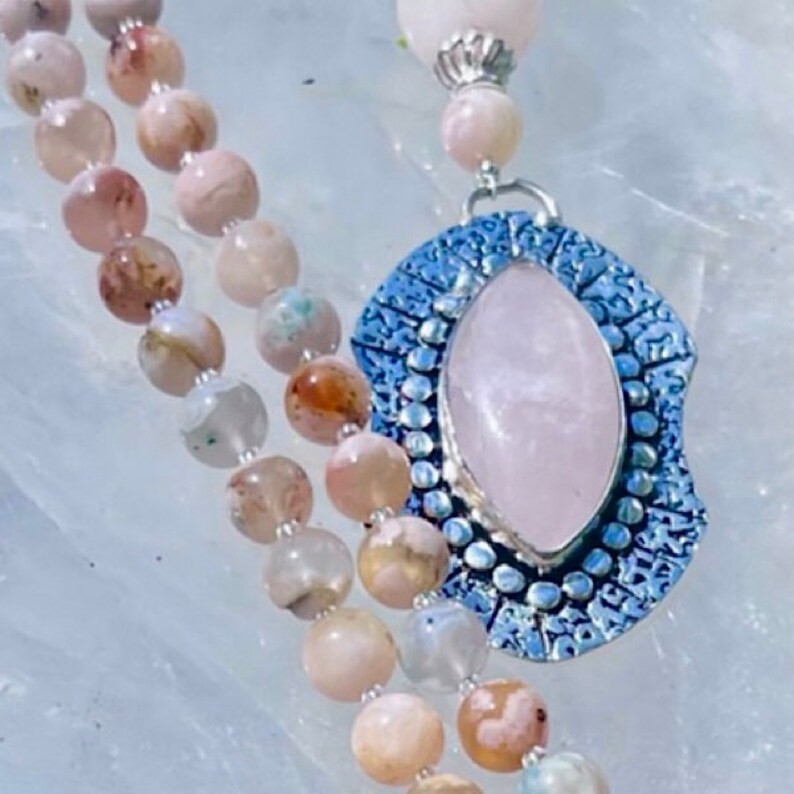 May include: A pink and white agate beaded necklace with a silver pendant featuring a large rose quartz stone.