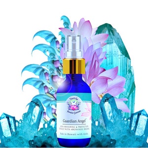 Puede incluir: Un frasco rociador de vidrio azul con una tapa dorada, etiquetado como "Guardian Angel". La botella está rodeada de cristales azul claro, flores de loto moradas y detalles florales azules. El texto de la etiqueta dice "Aura Shielding & Protection, Connect with Archangel Michael."