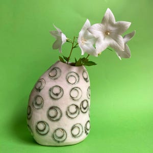 May include: A white ceramic vase with a textured pattern of circles in black and grey. The vase is filled with white flowers.