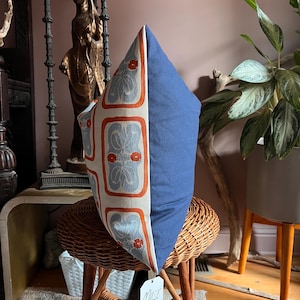 May include: A decorative pillow with a blue and floral patterned design. The pillow has a solid blue side and a patterned side with orange and gray floral motifs. The pillow is displayed on a wicker chair.