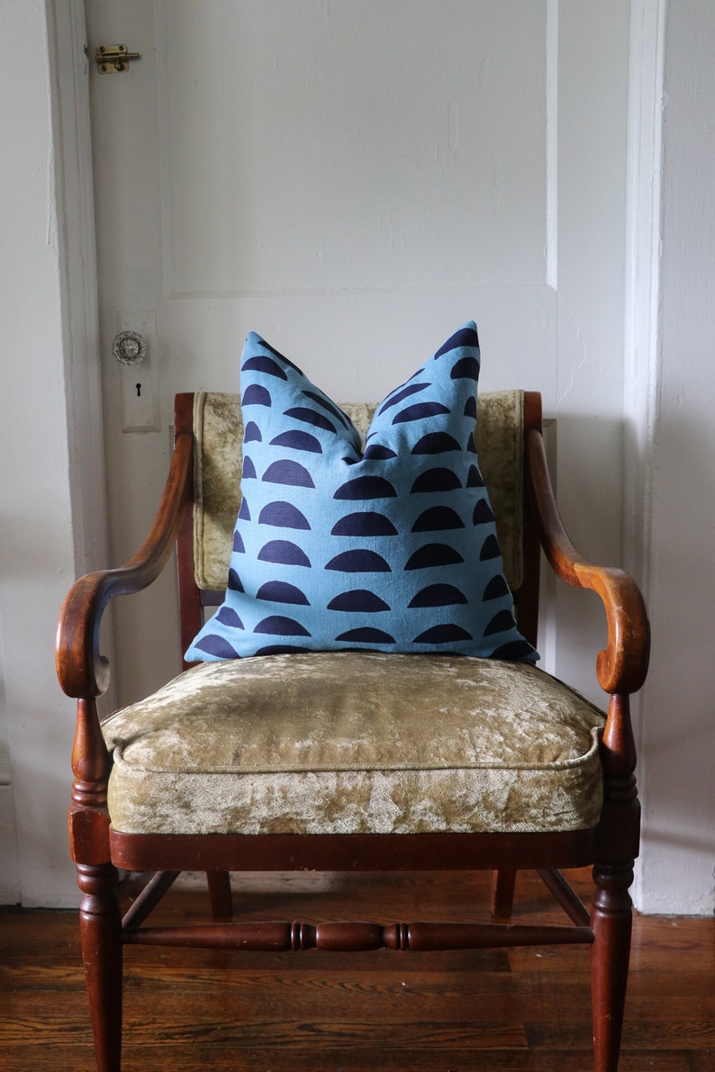 May include: A blue and navy patterned throw pillow sits on a brown velvet armchair with wooden arms and legs.