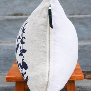 Pu&ograve; includere: Un cuscino decorativo con un design botanico. Il cuscino presenta un tessuto di lino con un motivo floreale blu navy su un lato e un tessuto bianco sull'altro. &Egrave; visibile una cerniera argentata con un tirante nero.