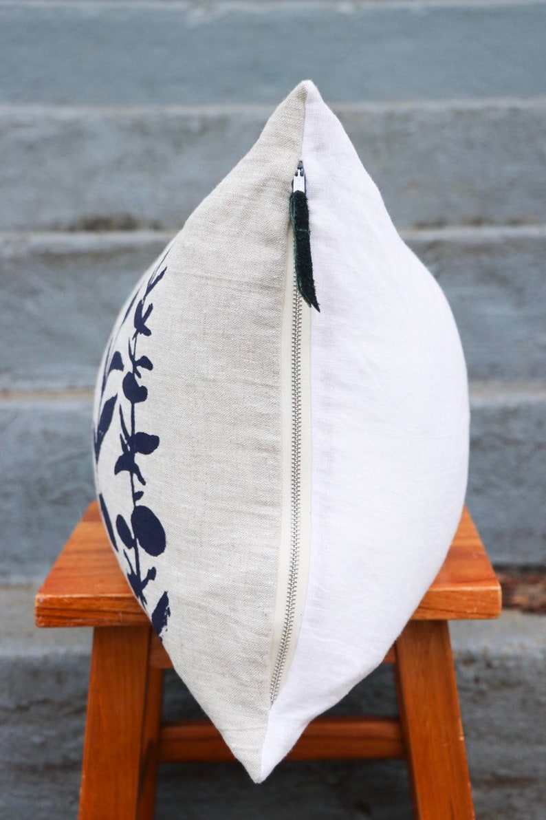 Pu&ograve; includere: Un cuscino decorativo con un design botanico. Il cuscino presenta un tessuto di lino con un motivo floreale blu navy su un lato e un tessuto bianco sull'altro. &Egrave; visibile una cerniera argentata con un tirante nero.