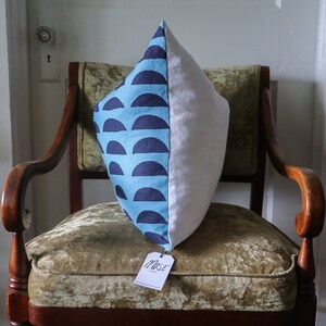 May include: A blue and white patterned pillow with a white tag that says "Muse" on a wooden chair with a green velvet seat.