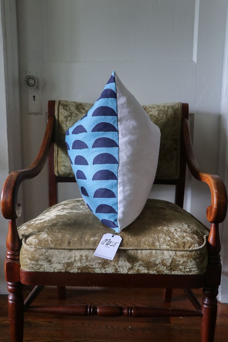 May include: A blue and white patterned pillow with a white tag that says "Muse" on a wooden chair with a green velvet seat.
