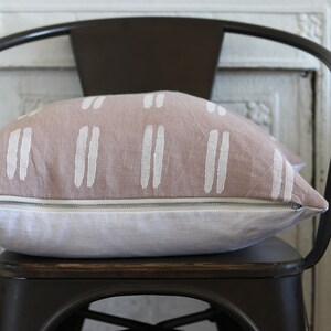 May include: A decorative pillow with a light brown top and white vertical stripe design. The bottom half of the pillow is white. The pillow is resting on a dark brown metal chair.