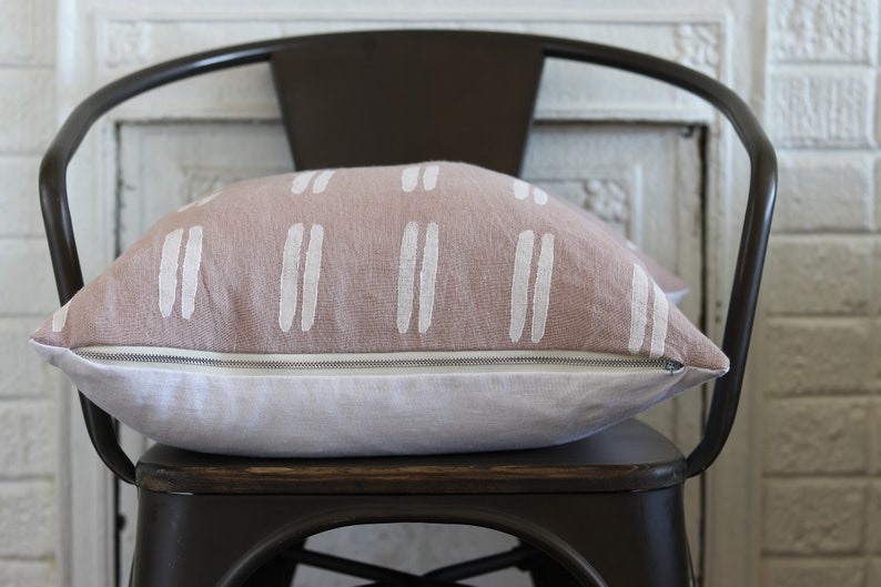May include: A decorative pillow with a light brown top and white vertical stripe design. The bottom half of the pillow is white. The pillow is resting on a dark brown metal chair.