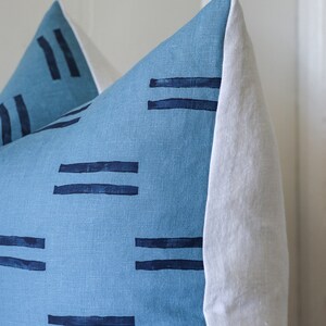 Puede incluir: Una almohada azul y blanca con un patr&oacute;n geom&eacute;trico de l&iacute;neas dobles. La almohada est&aacute; hecha de una tela suave y texturizada.